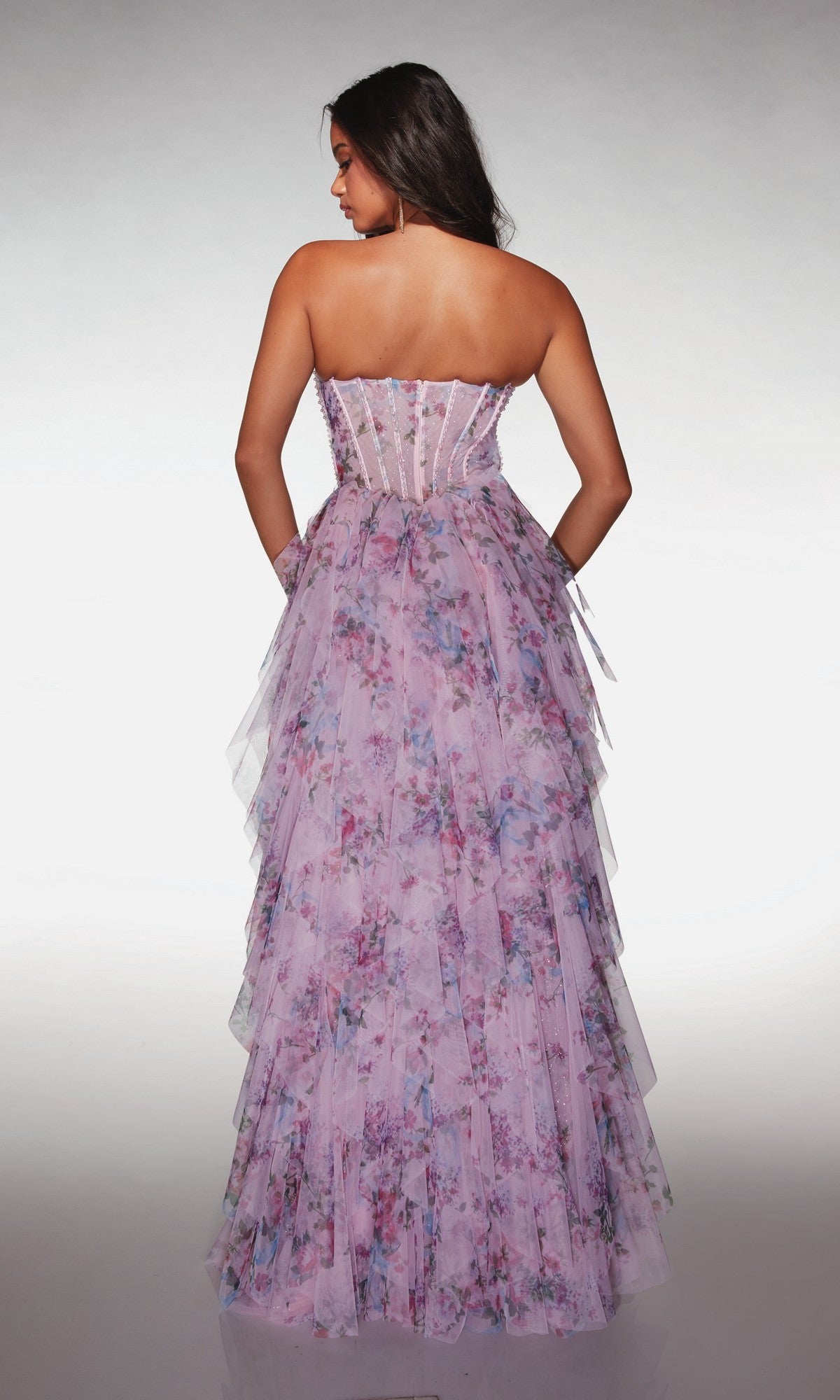 Woman wearing the Alyce 62041 long prom dress, a strapless, floor-length gown with a layered floral print in pink and purple hues, featuring a delicate corset bodice and shown from the back.